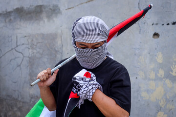 Man wearing a keffiyeh holds the Palestinian flag with hand on chest.