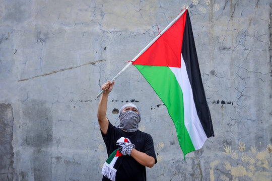 Young man waving the Palestine flag with hand on chest.