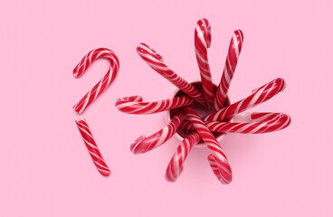 Cup with Christmas candy canes on pink background