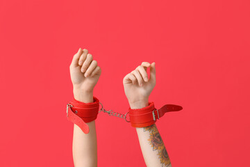 Female hands in handcuffs from sex shop on red background