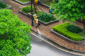 Aerial view of park with worker cleaning dirty street with high pressure cleaner