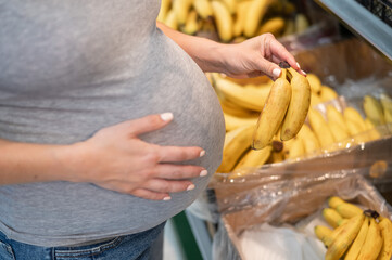 Pregnant woman buys bananas in the store. 