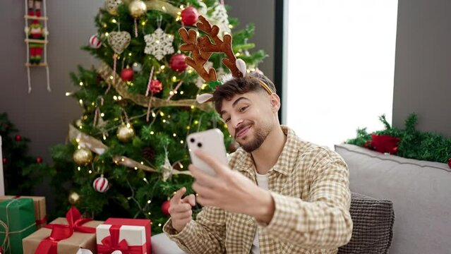 Young arab man make selfie by smartphone sitting by christmas tree at home