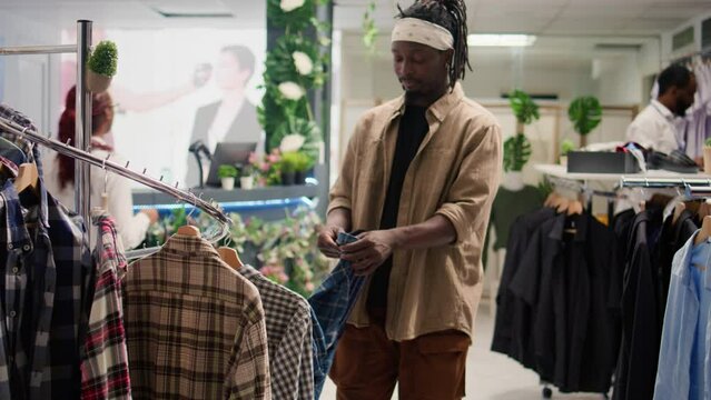 Client browsing through wares in mall clothing store during promotional season, looking to buy clothes to fill his wardrobe. Man taking advantage of sales in fashion boutique, looking at cozy shirts