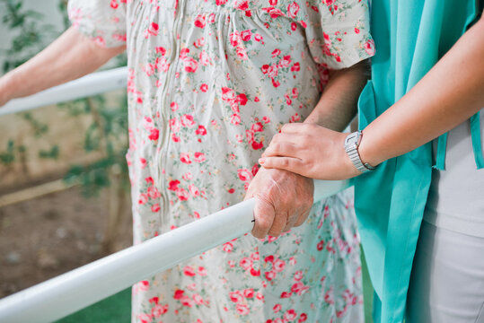 Physiotherapist or specialized physician holding hand of patient using parallel bars to practice walking.