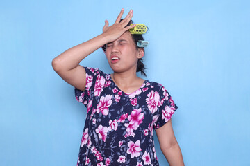 Upset Asian housewife wear hair curlers slapping forehead with palm and showing worried or regret expression - obrazy, fototapety, plakaty