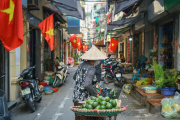 Obraz premium Woman vendor selling fruits on Hanoi street. Vietnamese flags on background