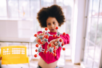 Little girl having fun holding a molecular model learning chemistry science in the classroom....