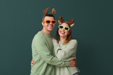 Beautiful young couple in reindeer horns and sunglasses on green background