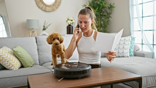 Young caucasian woman with dog reading cleaner vacuum robot instructions talking on smartphone at home