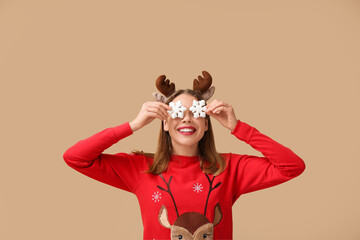 Beautiful young woman in reindeer horns with decorative snowflakes on beige background