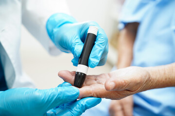 Asian doctor using lancet pen on senior patient finger for check sample blood sugar level to...