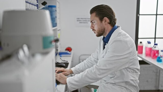 Young hispanic man scientist using computer smiling at laboratory