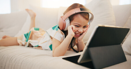 Happy little girl, tablet and headphones on sofa for elearning, entertainment or streaming at home....