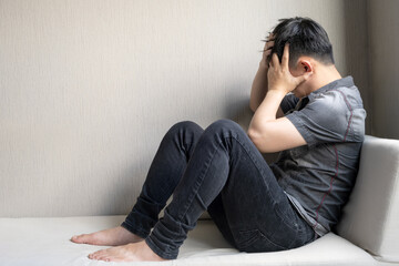 Man has a headache and is stressed, he sits on the sofa at home. He held his head in his hands and his face was unhappy. Causes of working hard and not getting enough rest