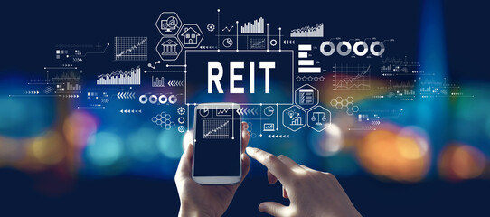 REIT - Real Estate Investment Trust theme with person using a smartphone in a city at night