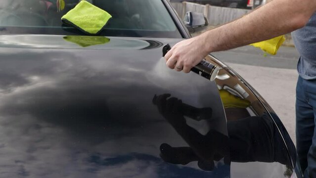 Applying a spray sealant to a black car bonnet hood