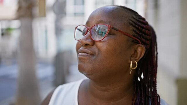 African american woman finds calm in a busy city, standing eyes closed, taking a deep breath on an urban street, enjoying the summer sun