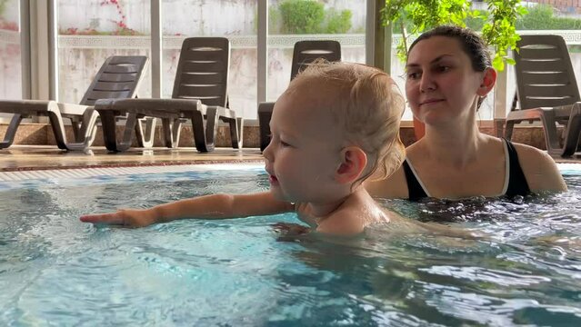 mother and little daughter swim and have fun in the pool. the child splashes a lot of water on his mother. Filmed in Bulgaria in Banya. High-quality shooting in 4K format