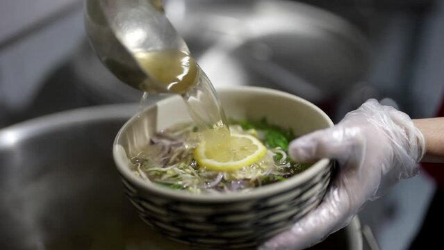 chef cooking traditional Vietnamese soup Pho-Bo, pouring tasty hot broth into bowl with rice noodles