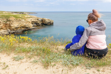 Fototapeta premium A girl with a child on Cape Tarkhankut. The rocky coast of the Dzhangul Reserve in the Crimea. Turquoise sea water. Rocks and grottoes of Cape Tarkhankut on the Crimean peninsula.