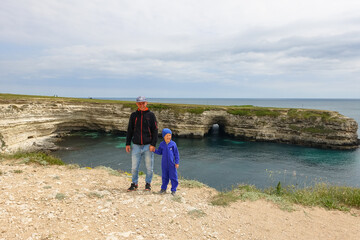 A man with a child on Cape Tarkhankut. The rocky coast of the Dzhangul Reserve in the Crimea. Turquoise sea water. Rocks and grottoes of Cape Tarkhankut on the Crimean peninsula.