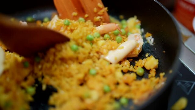 Spanish cook cooking traditional paella with rice and seafood, stirring ingredients on hot pan