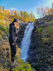 A girl on the background of a beautiful waterfall in the autumn mountains beyond the Arctic Circle in the north, in Khibiny, Murmansk region. Kola Peninsula