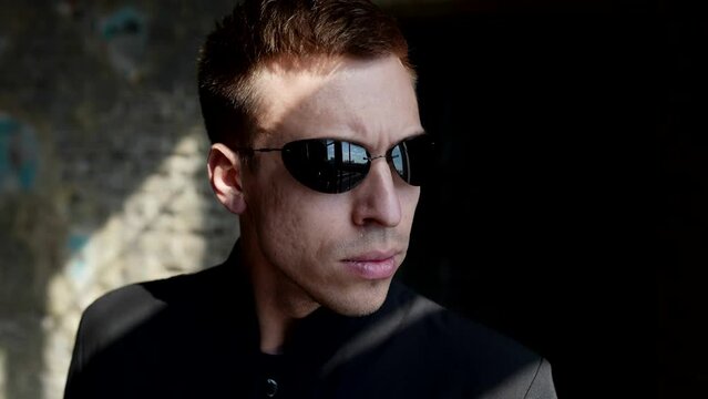 portrait of serious man with black sunglasses standing indoor and looking at window, closeup view