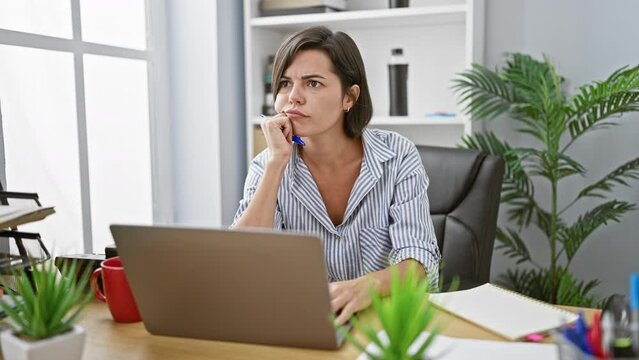 Young and beautiful hispanic woman worker, concentrating on her laptop, sparks a brilliant business idea in the vibrant office interior