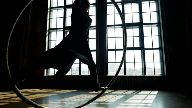 man in black dancing crazy dance with hoop in hall, silhouette against window, slow motion