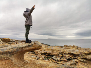 A boy on the shore of red stones next to the rocks of Two brothers on the Fishing Peninsula. The...