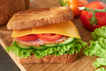 Delicious sandwich with cheese, tomato and cucumber on wooden board