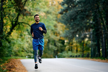 Happy athlete listening music on earbuds while jogging on road.