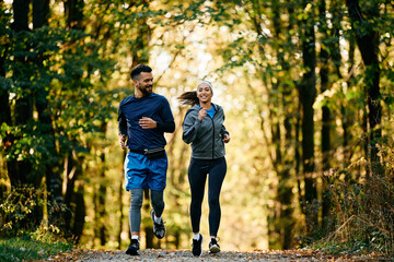 Happy sports couple jogging through autumn park.