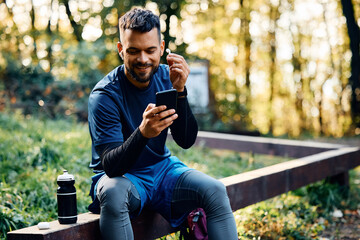 Happy athlete using smart phone and earbuds while exercising in park.