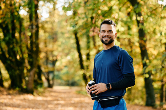 Happy athletic man with water bottle in park looking at camera.