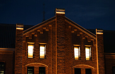 The night sky in the background and the brick wall and lighted windows of the old building at night