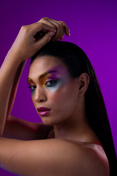 Vertical image of biracial woman with dark hair, pink lips, eyeshadow make up on purple background