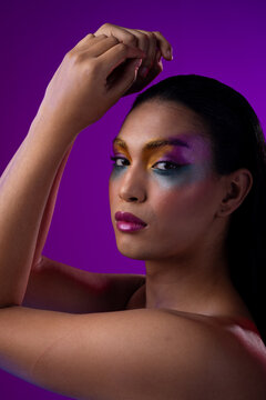 Vertical image of biracial woman with dark hair, pink lips, eyeshadow make up on purple background