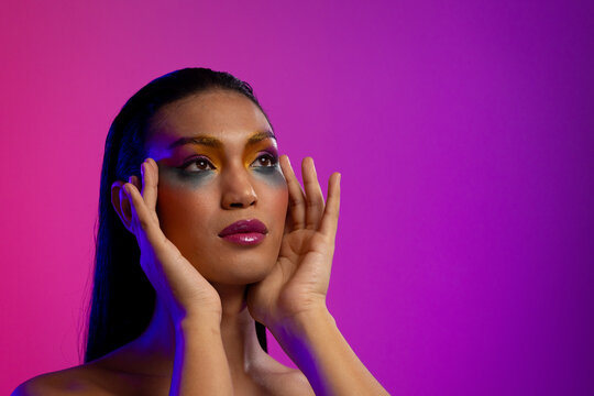 Biracial woman with dark hair, hands to head, pink lips, eyeshadow make up on purple background