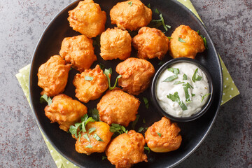Hush puppies is made with eggs, onion, self-rising flour, and cornmeal, then deep-fried until crisp and golden closeup on the plate on the table. Horizontal top view from above