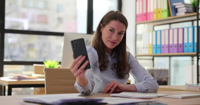 Young business woman secretary takes selfie on mobile phone in office