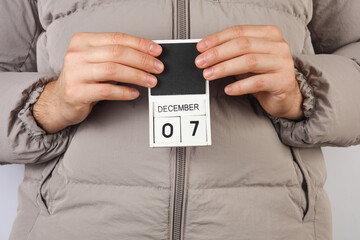 Man in down jacket holds wooden block calendar with date December 7