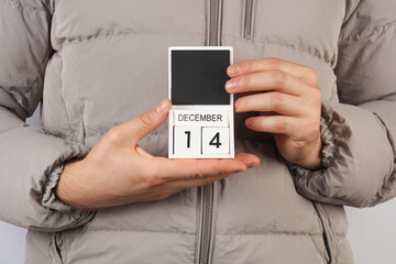 Man in down jacket holds wooden block calendar with date December 14