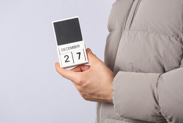 Man in down jacket holds wooden block calendar with date December 27