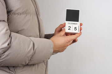 Man in down jacket holds wooden block calendar with date December 25