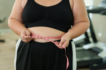 Close-up of Chubby woman's waist Exercise in fitness center using tape measure around waist. very glad able to lose weight and make waist smaller. After running on treadmill in attempt to lose weight