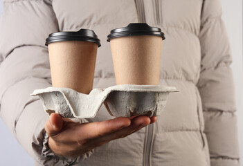 Man in down jacket holds coffee cups in tray on a gray background
