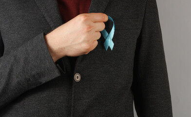 Businessman in a suit jacket holding  blue prostate cancer awareness ribbon